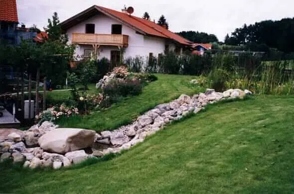 Bachlauf aus Natursteinen und Findlingen in einem Rasengarten