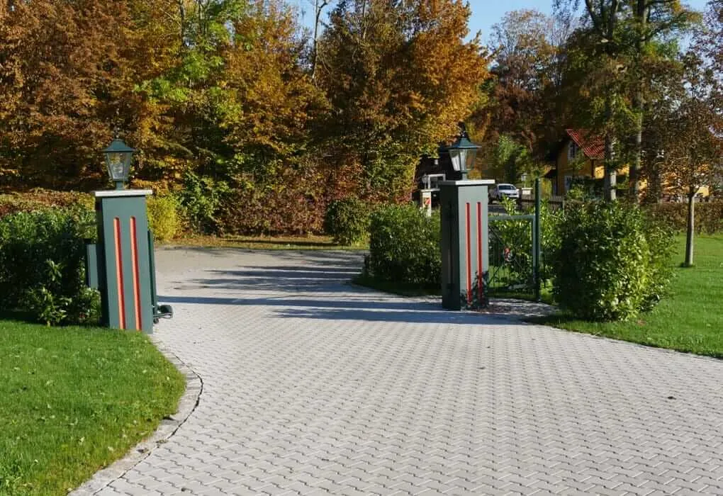 Breite gepflasterte Auffahrt zwischen zwei Torpfeilern